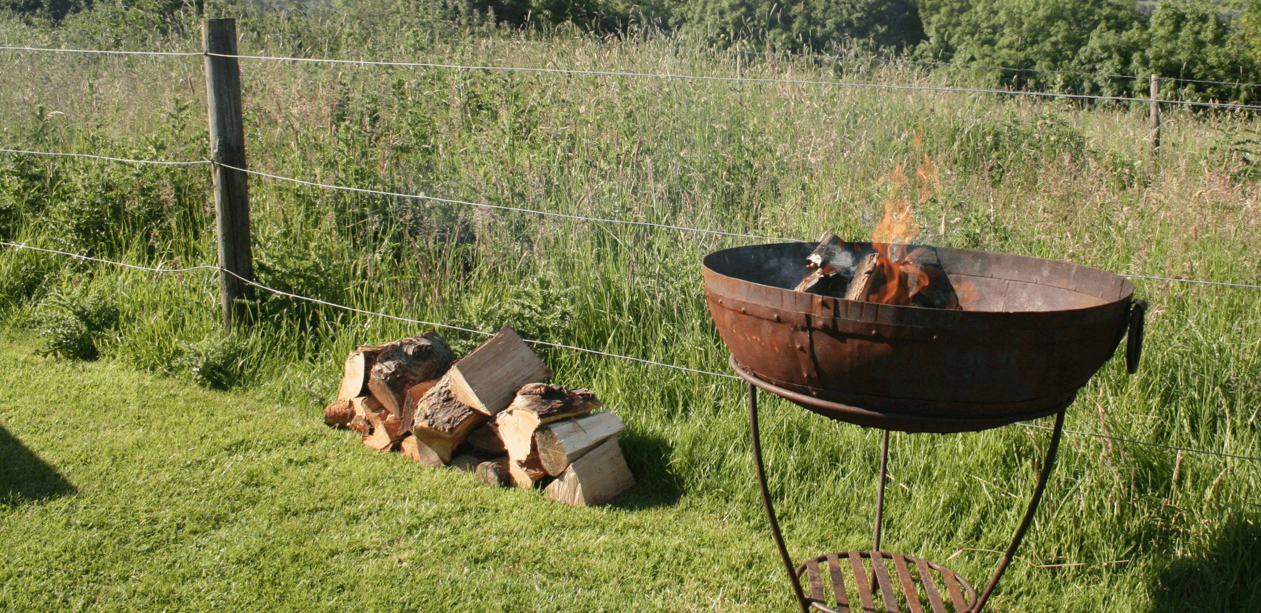 Pile of logs next to fire pit with a lit fire